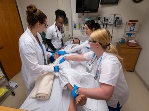 team of nursing students and professor holding simulation patient